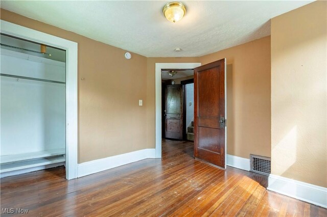 unfurnished bedroom featuring baseboards, a closet, hardwood / wood-style flooring, and visible vents