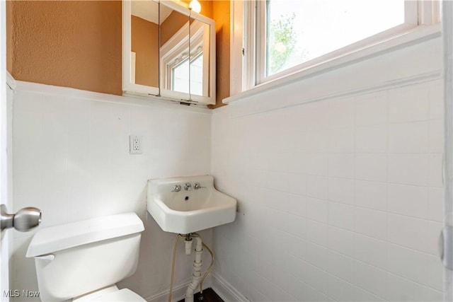 bathroom with toilet, tile walls, wainscoting, and a sink