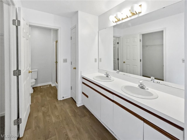 full bath featuring double vanity, a sink, wood finished floors, and toilet