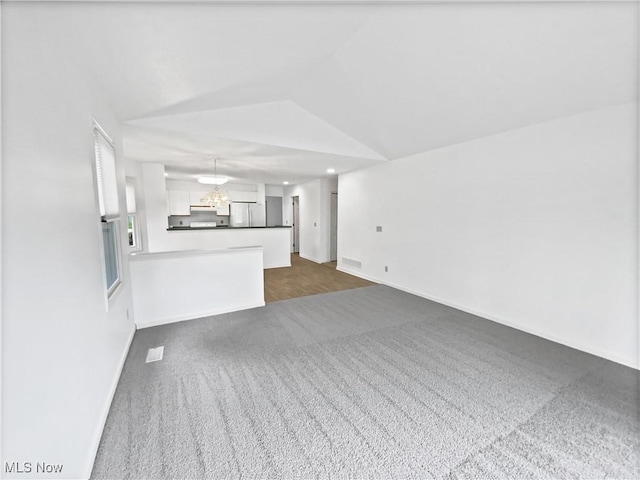 unfurnished living room featuring visible vents, an inviting chandelier, dark carpet, baseboards, and vaulted ceiling