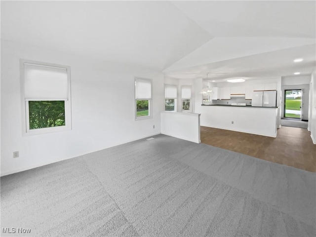 unfurnished living room with a chandelier, a wealth of natural light, lofted ceiling, and dark colored carpet