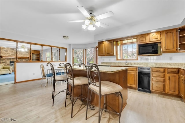 kitchen with a ceiling fan, black microwave, light wood-style flooring, and a kitchen bar