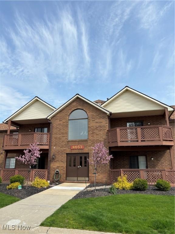 view of front facade with brick siding, a balcony, and a front yard