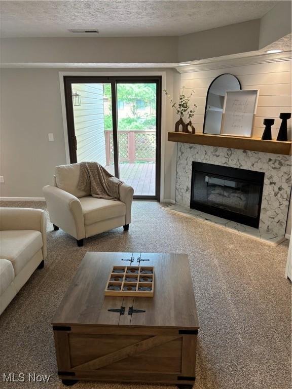 living room featuring carpet floors, baseboards, a fireplace, and a textured ceiling