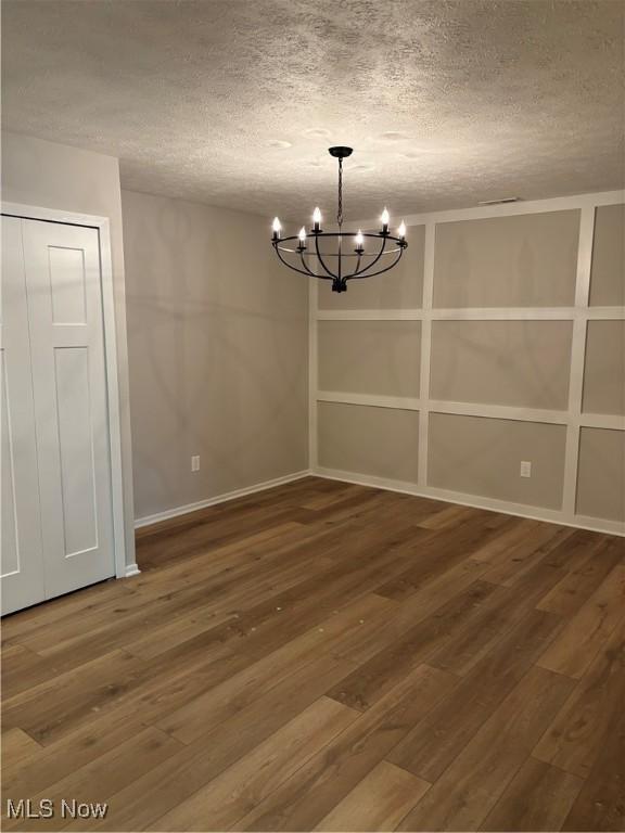 unfurnished dining area featuring wood-type flooring, a textured ceiling, and a chandelier