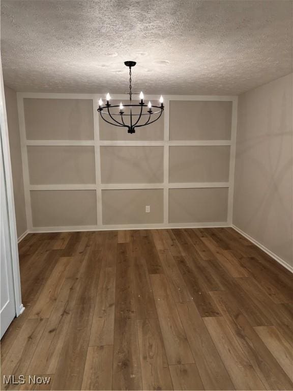 unfurnished dining area featuring an inviting chandelier, a textured ceiling, and wood finished floors