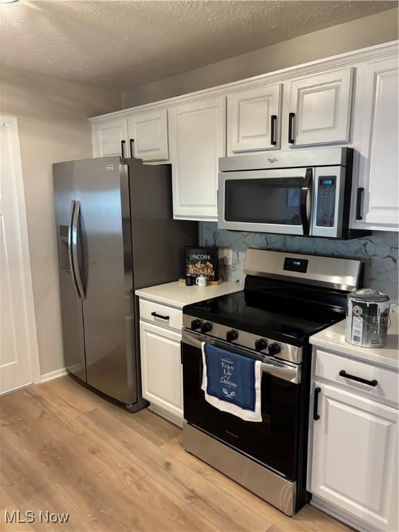 kitchen featuring light countertops, white cabinets, stainless steel appliances, and light wood-style flooring