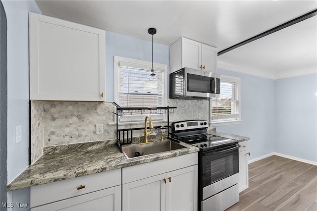 kitchen with white cabinets, a sink, light wood finished floors, stainless steel appliances, and tasteful backsplash