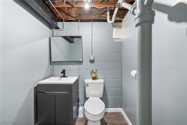 half bath featuring vanity, toilet, concrete block wall, baseboards, and wood finished floors