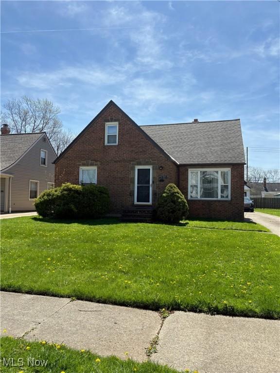 view of front of house with brick siding, a shingled roof, and a front lawn
