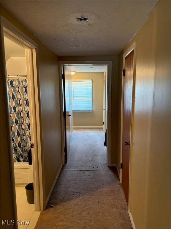 corridor with baseboards and light carpet
