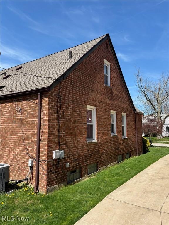 view of property exterior featuring a yard, brick siding, central AC unit, and roof with shingles