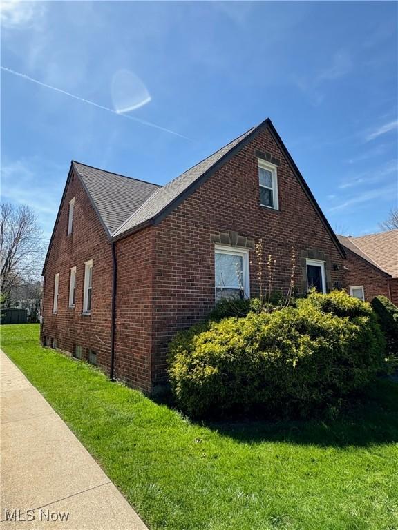 view of side of property with a yard, brick siding, and a shingled roof