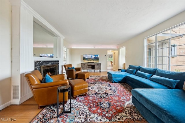 living area featuring a high end fireplace, a healthy amount of sunlight, wood finished floors, and visible vents