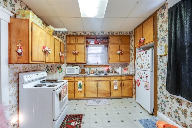 kitchen with white appliances, a drop ceiling, a sink, and light floors