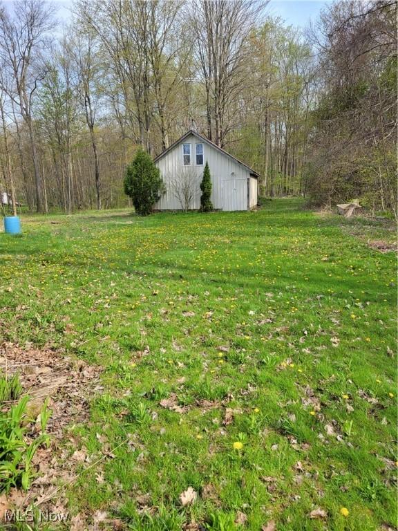 view of yard featuring a pole building, a wooded view, and an outbuilding