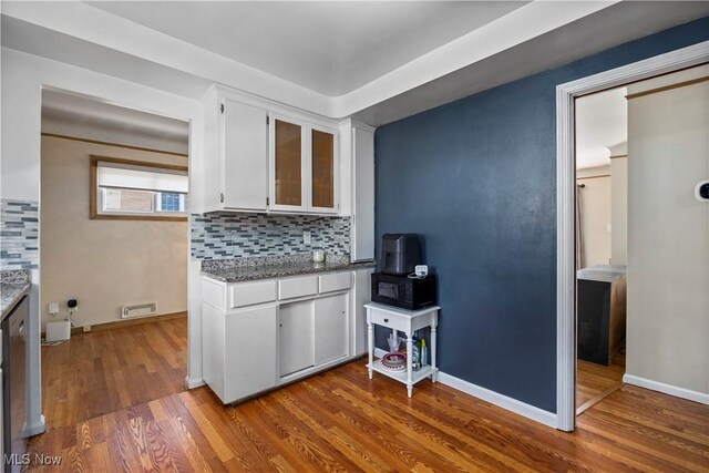 kitchen with wood finished floors, black microwave, glass insert cabinets, white cabinets, and tasteful backsplash
