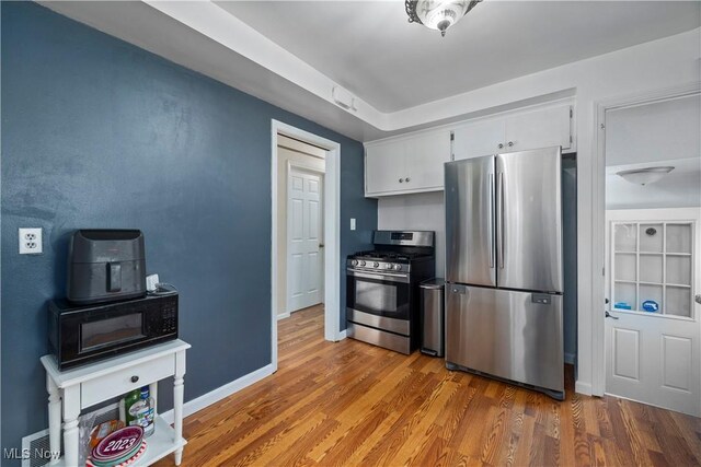 kitchen featuring baseboards, appliances with stainless steel finishes, wood finished floors, and white cabinets
