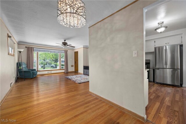unfurnished living room featuring baseboards, wood finished floors, and ceiling fan with notable chandelier