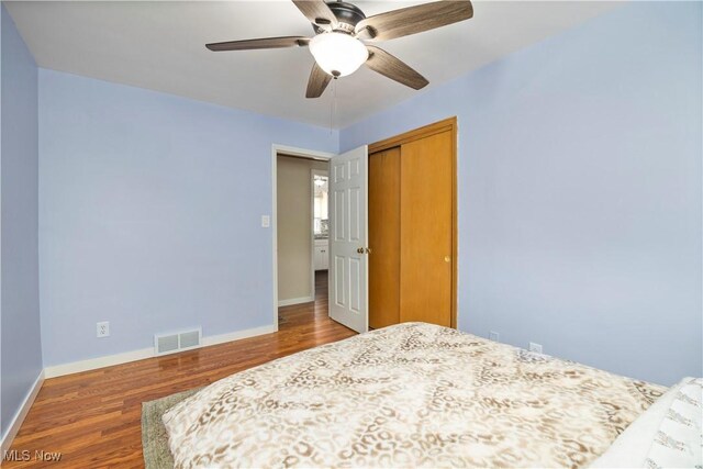 bedroom featuring ceiling fan, baseboards, wood finished floors, visible vents, and a closet