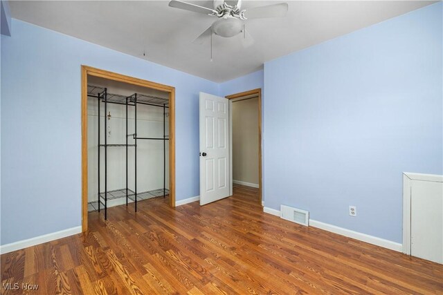 unfurnished bedroom featuring a ceiling fan, visible vents, wood finished floors, baseboards, and a closet