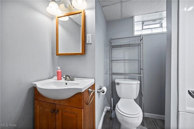 bathroom with vanity, wood finished floors, toilet, baseboards, and a drop ceiling