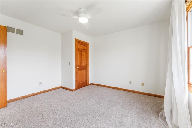 carpeted spare room with baseboards, ceiling fan, and visible vents