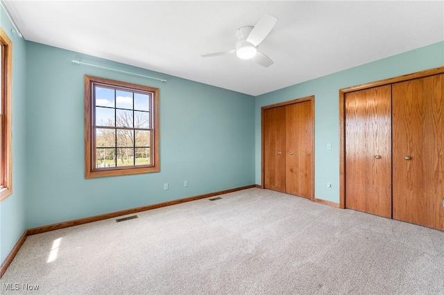 unfurnished bedroom featuring baseboards, carpet, two closets, and visible vents