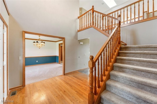 stairs featuring baseboards, a chandelier, wood finished floors, and a towering ceiling