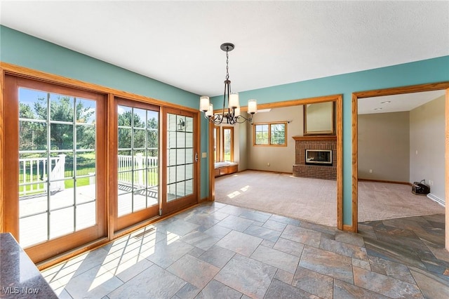 unfurnished dining area featuring a fireplace, baseboards, stone tile flooring, a notable chandelier, and carpet flooring