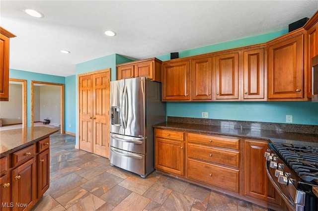 kitchen featuring stone tile flooring, brown cabinetry, dark stone countertops, and stainless steel appliances