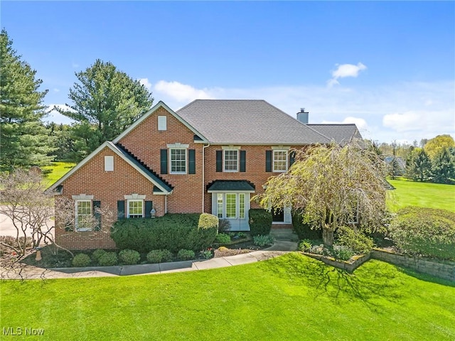 colonial home featuring brick siding, a chimney, and a front lawn