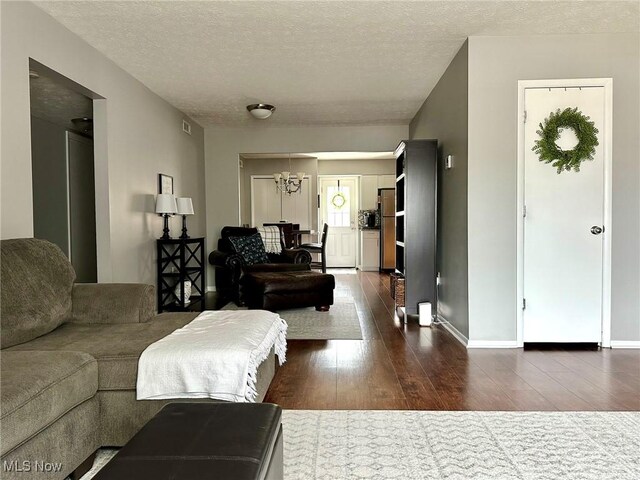 living room with dark wood-type flooring, a textured ceiling, baseboards, and a notable chandelier