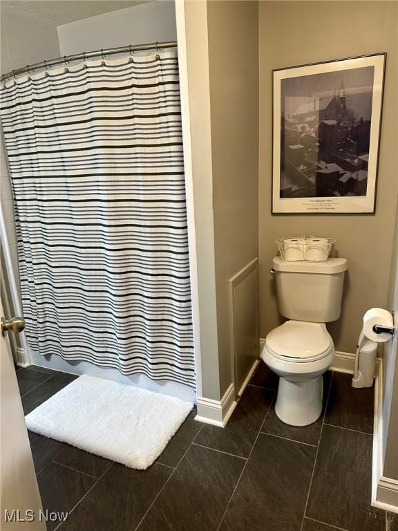 bathroom with a shower with shower curtain, toilet, tile patterned floors, and baseboards