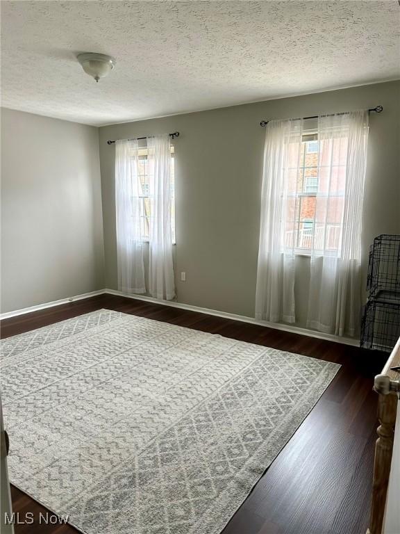 unfurnished room featuring baseboards, a textured ceiling, and dark wood-type flooring