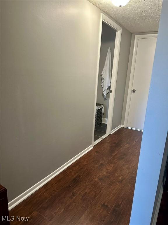hall featuring a textured ceiling, baseboards, and dark wood-type flooring