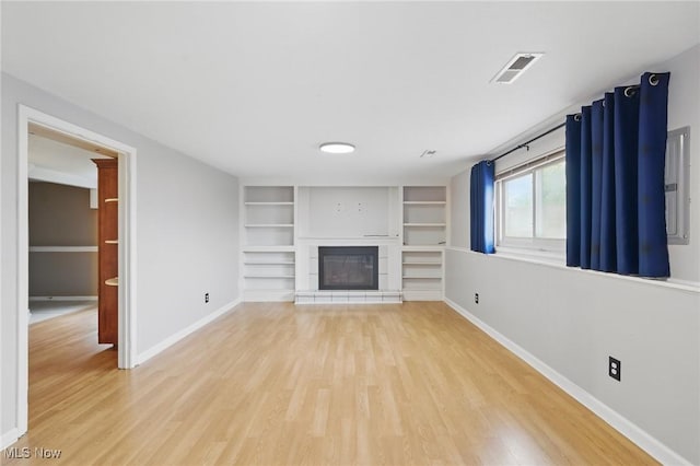 unfurnished living room with baseboards, light wood finished floors, a glass covered fireplace, and visible vents