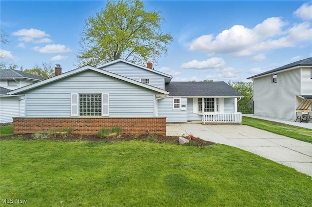 view of front of property featuring brick siding, a front yard, a chimney, covered porch, and driveway