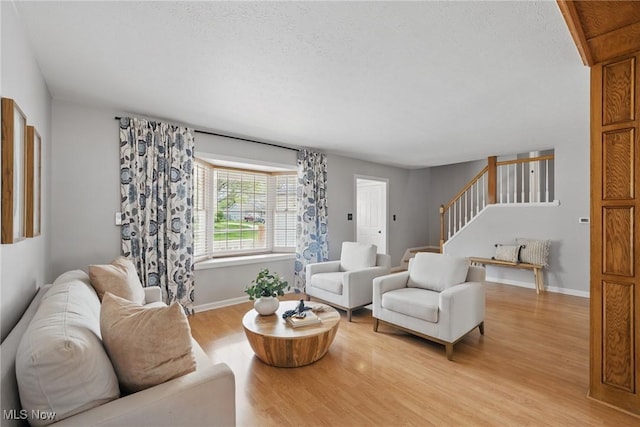 living area with stairs, baseboards, and light wood finished floors