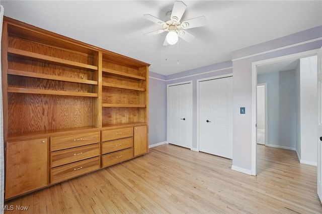unfurnished bedroom featuring multiple closets, baseboards, ceiling fan, and light wood-type flooring