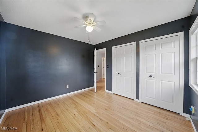 unfurnished bedroom featuring baseboards, multiple closets, ceiling fan, and light wood-type flooring