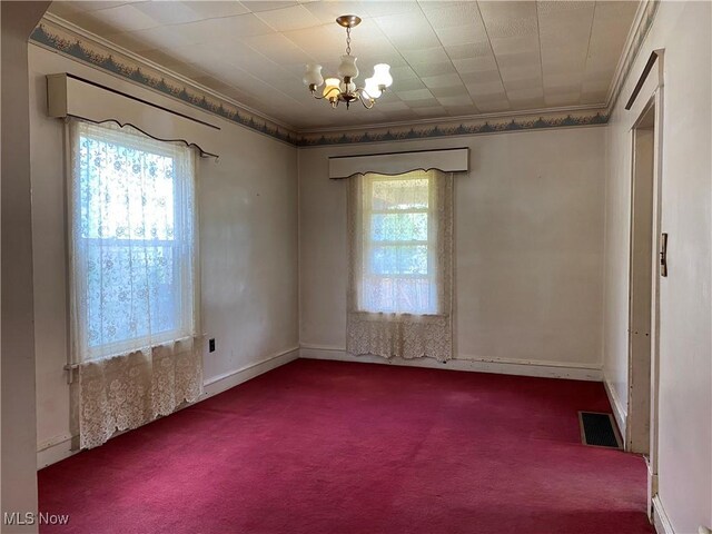 unfurnished room with carpet floors, ornamental molding, a healthy amount of sunlight, and an inviting chandelier