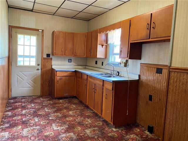 kitchen with light countertops, wallpapered walls, brown cabinetry, and a sink