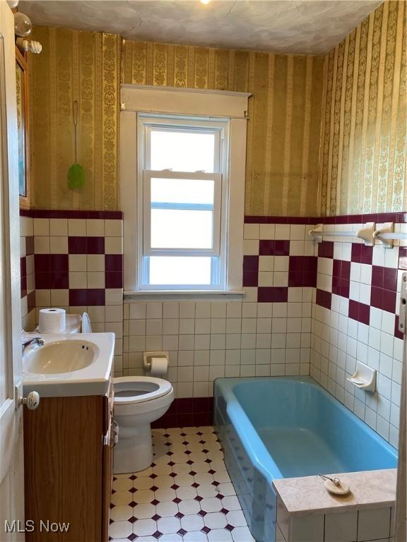 full bathroom with tile walls, toilet, wallpapered walls, and a bath