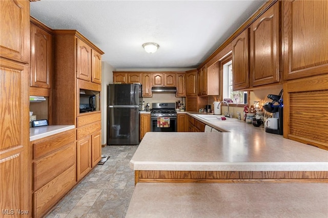 kitchen featuring stainless steel range with gas stovetop, a sink, light countertops, freestanding refrigerator, and a peninsula