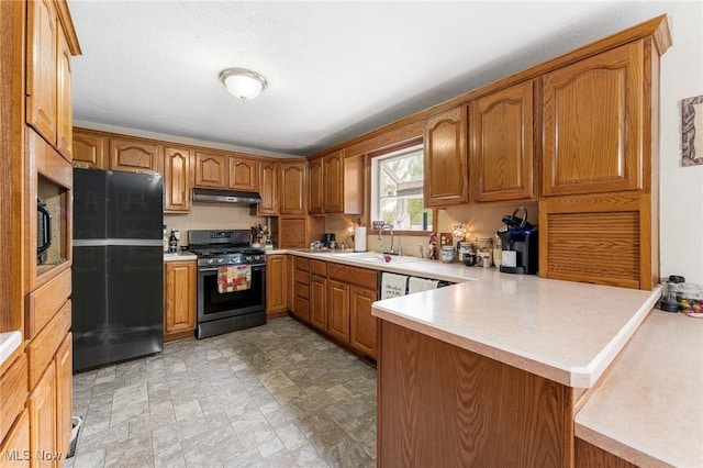kitchen with a sink, stainless steel gas stove, freestanding refrigerator, a peninsula, and under cabinet range hood
