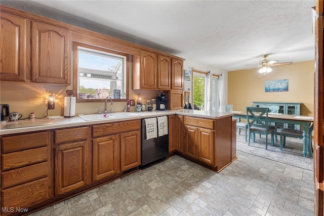 kitchen featuring brown cabinetry, a sink, dishwashing machine, and a peninsula