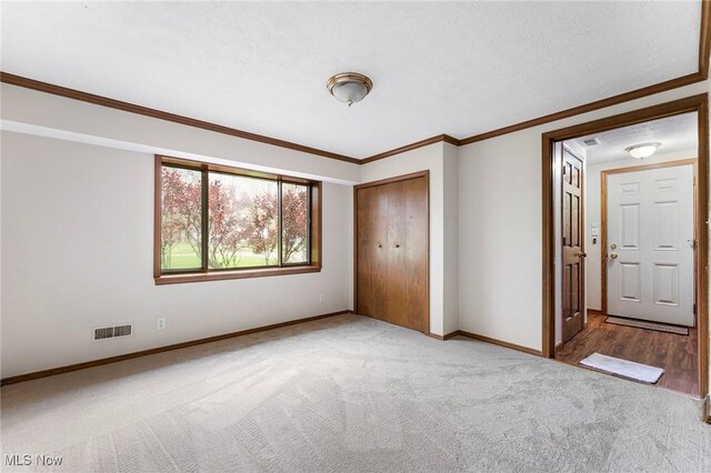 unfurnished bedroom with carpet flooring, baseboards, visible vents, ornamental molding, and a closet