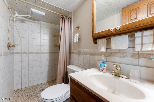 bathroom with vanity, a textured ceiling, toilet, and tiled shower
