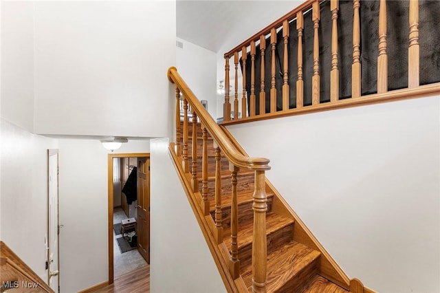 stairs with visible vents, wood finished floors, and a towering ceiling